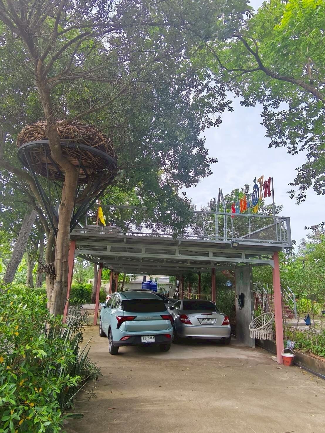 A parking area with two cars, a covered structure, and a tree with a nest.
