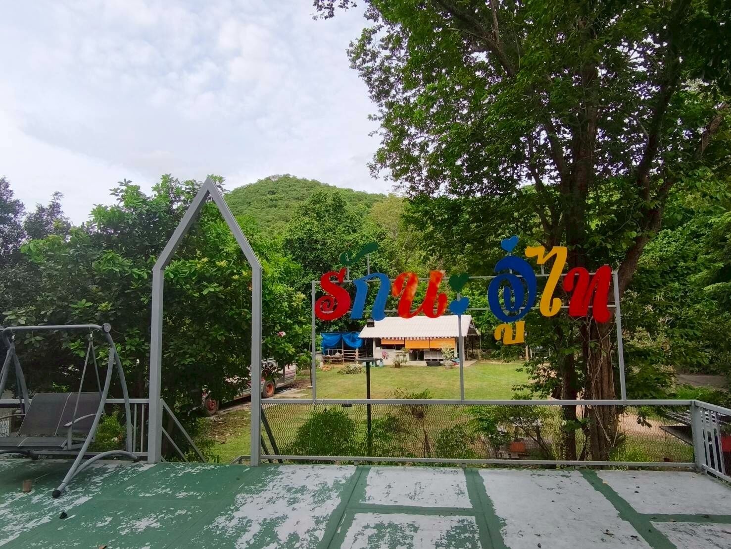 A playground with a metal frame and green surface, surrounded by trees and a hill in the background.