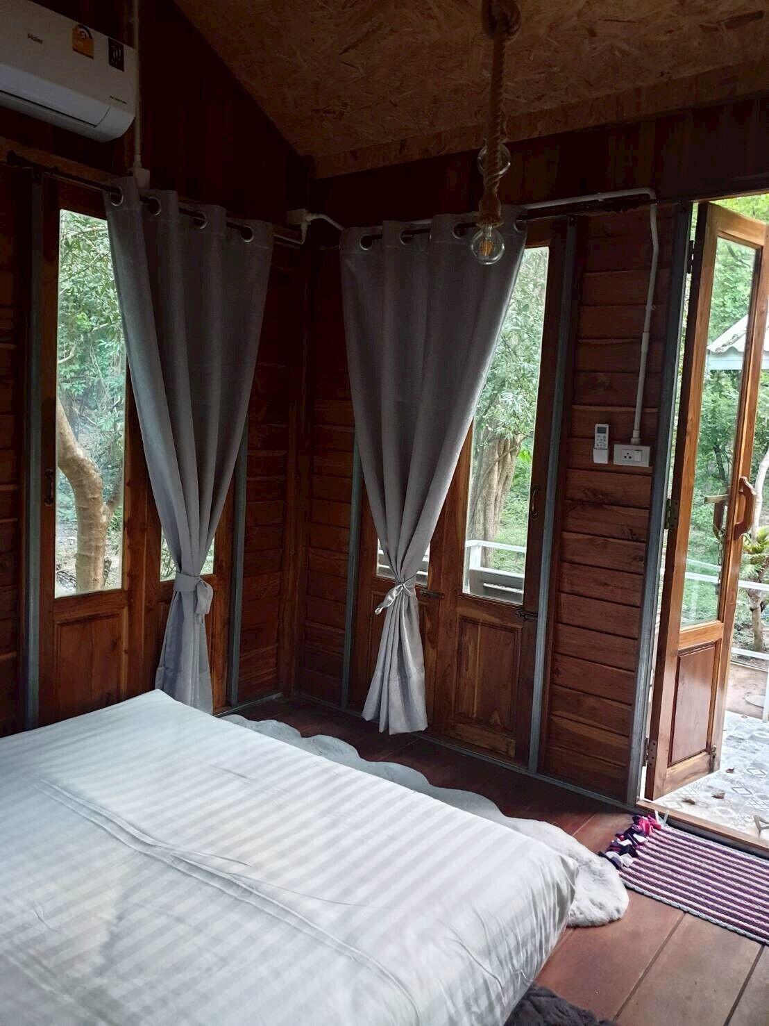 A wooden cabin bedroom with a bed, curtains, and a view of the outdoors.