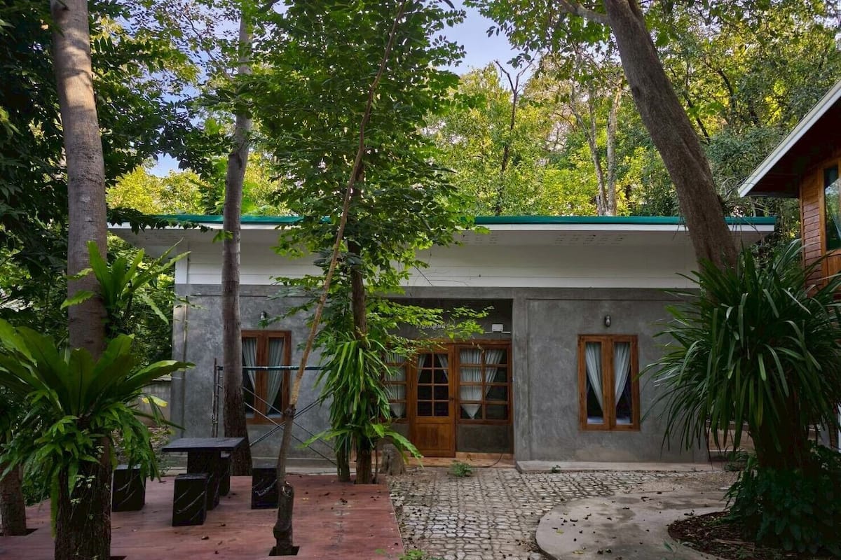 A house with a paved courtyard, a wooden door, and a window with curtains.