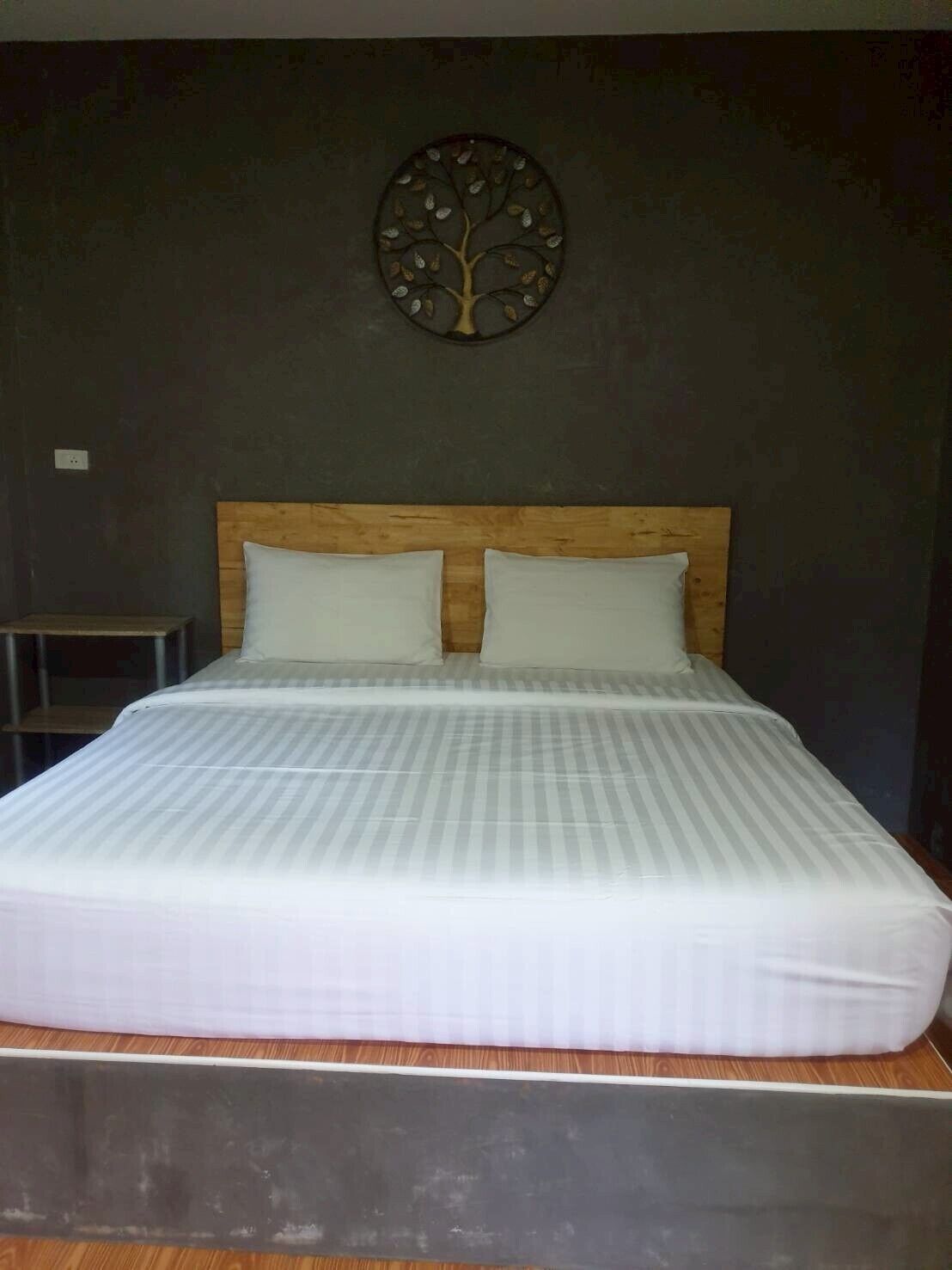 A bed with a wooden headboard, two pillows, and a wall-mounted tree decoration.