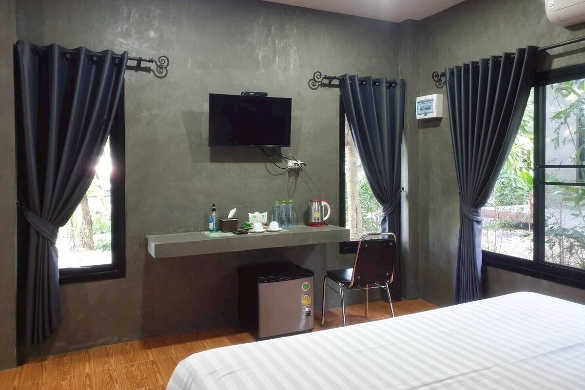 A hotel room with a bed, a desk with a television, a chair, and a window with curtains.