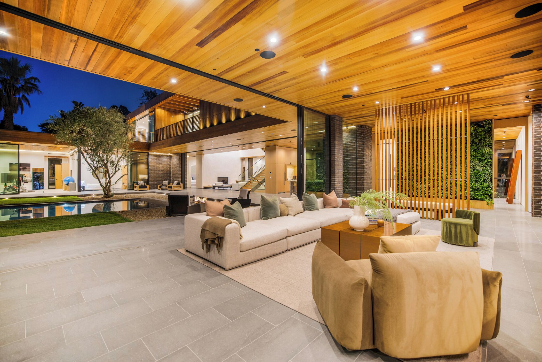 A modern living room with a sectional sofa, a coffee table, and a dining area with a glass partition.