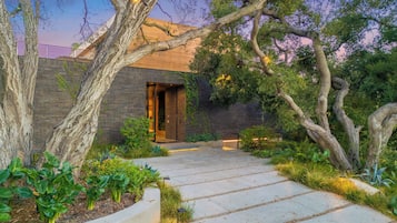 A modern building with a brick facade, a concrete pathway, and surrounding greenery.