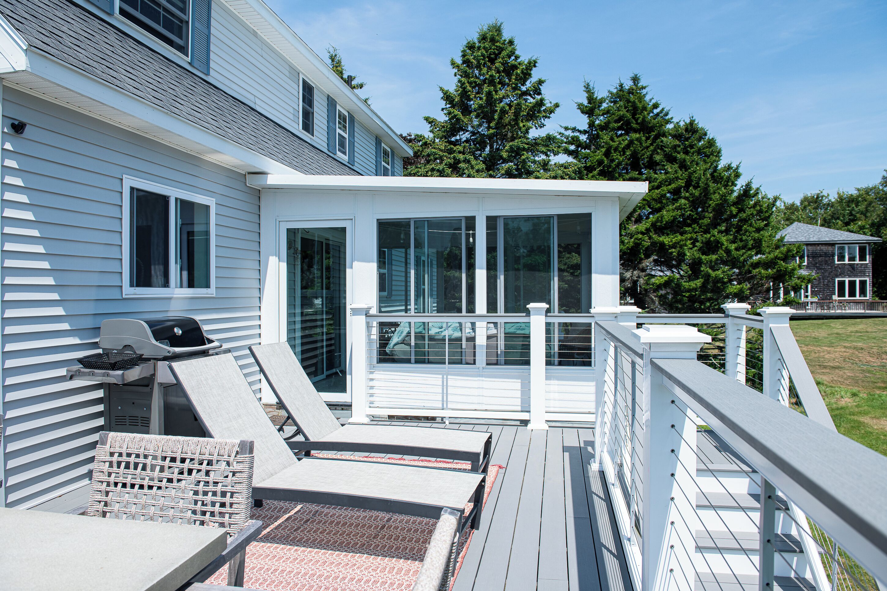 Eine Terrasse mit Grill, Liegestühlen und einer Glaskonstruktion.