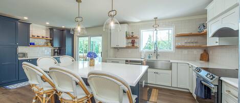 A modern kitchen with a central island, white cabinetry, and wicker chairs.