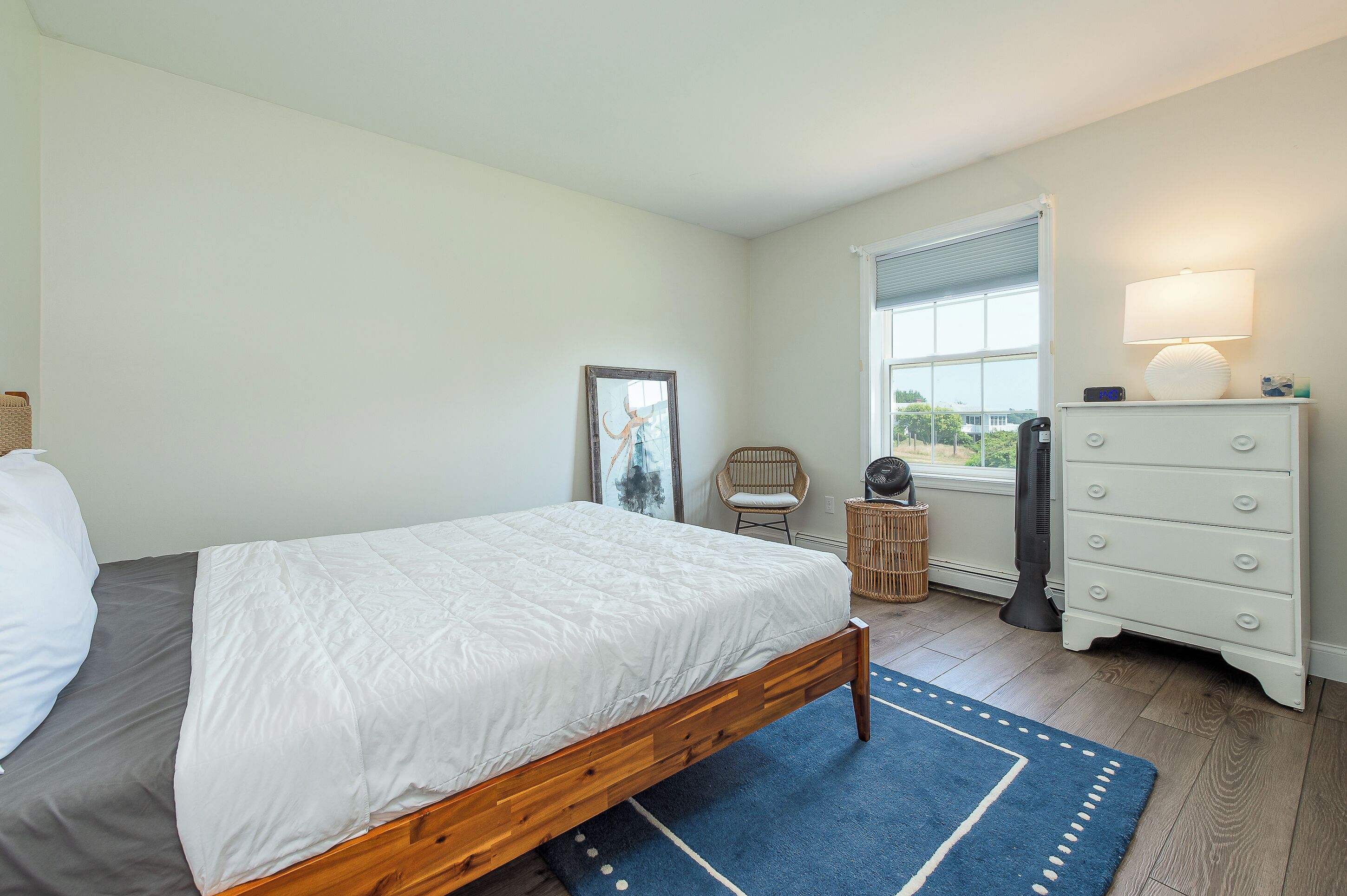 A bedroom with a bed, a dresser, a chair, a lamp, and a window.