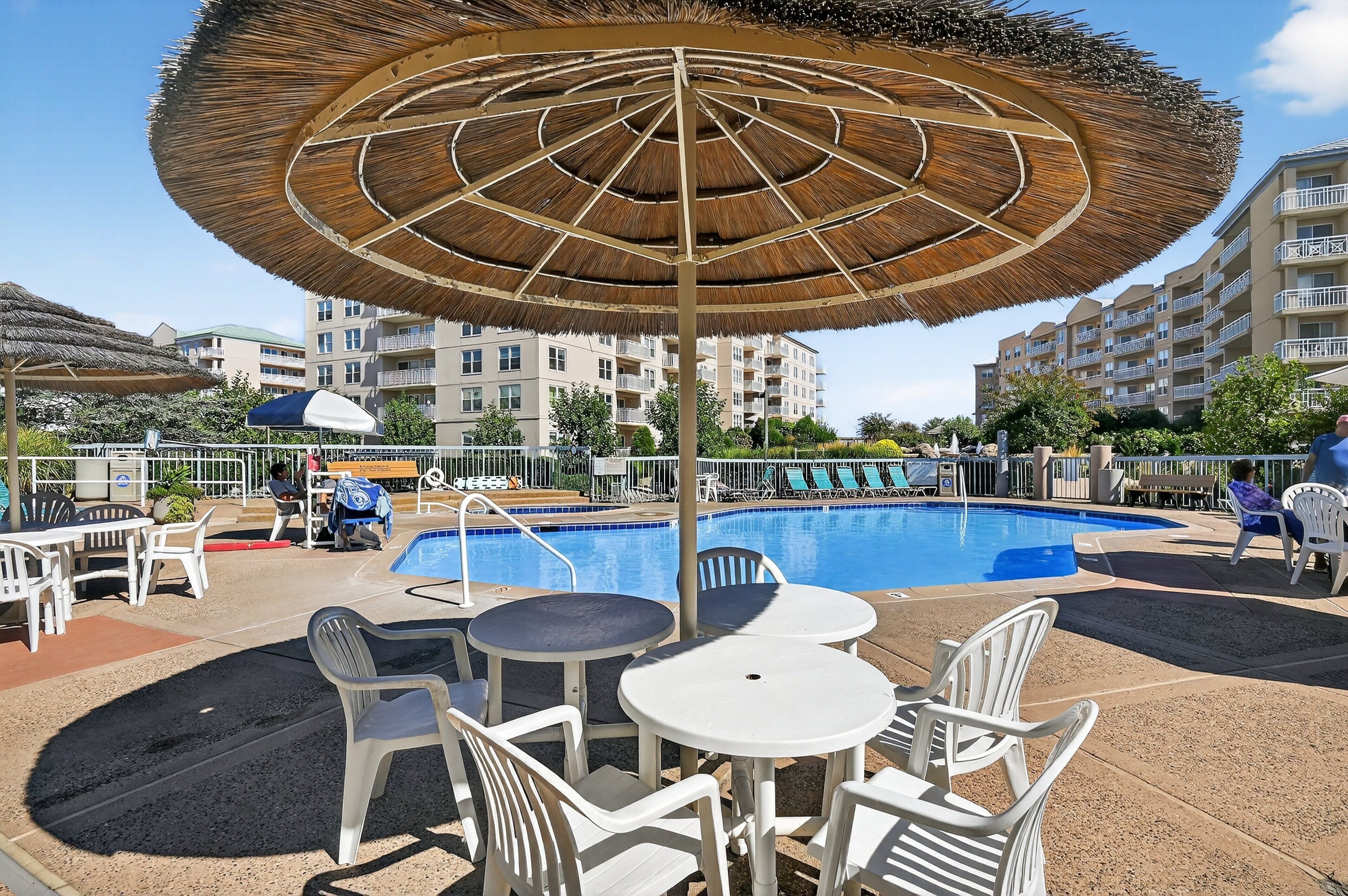 A poolside area with a large umbrella, lounge chairs, and a swimming pool.