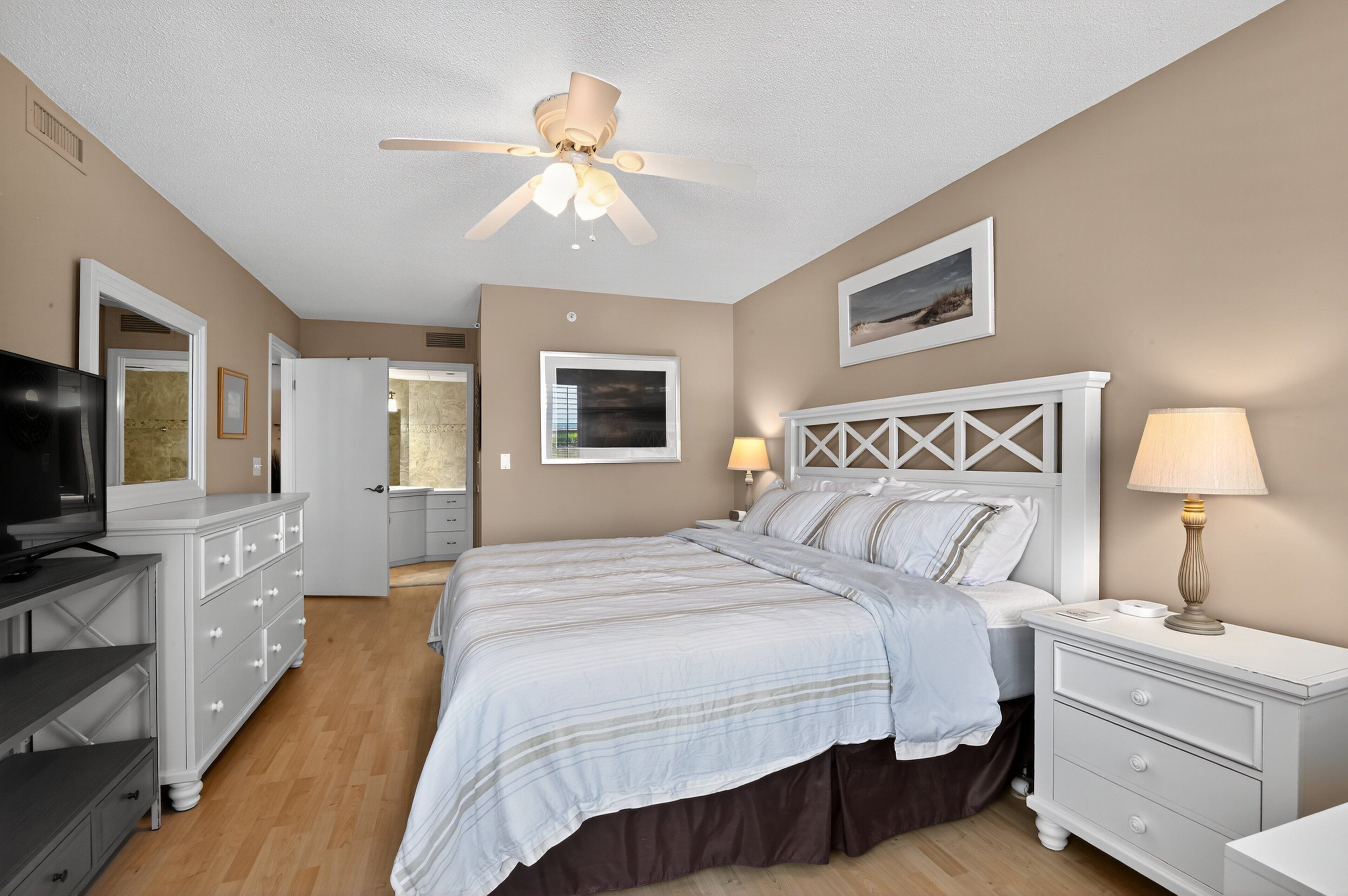A bedroom with a bed, nightstands, a dresser, a ceiling fan, and a television.