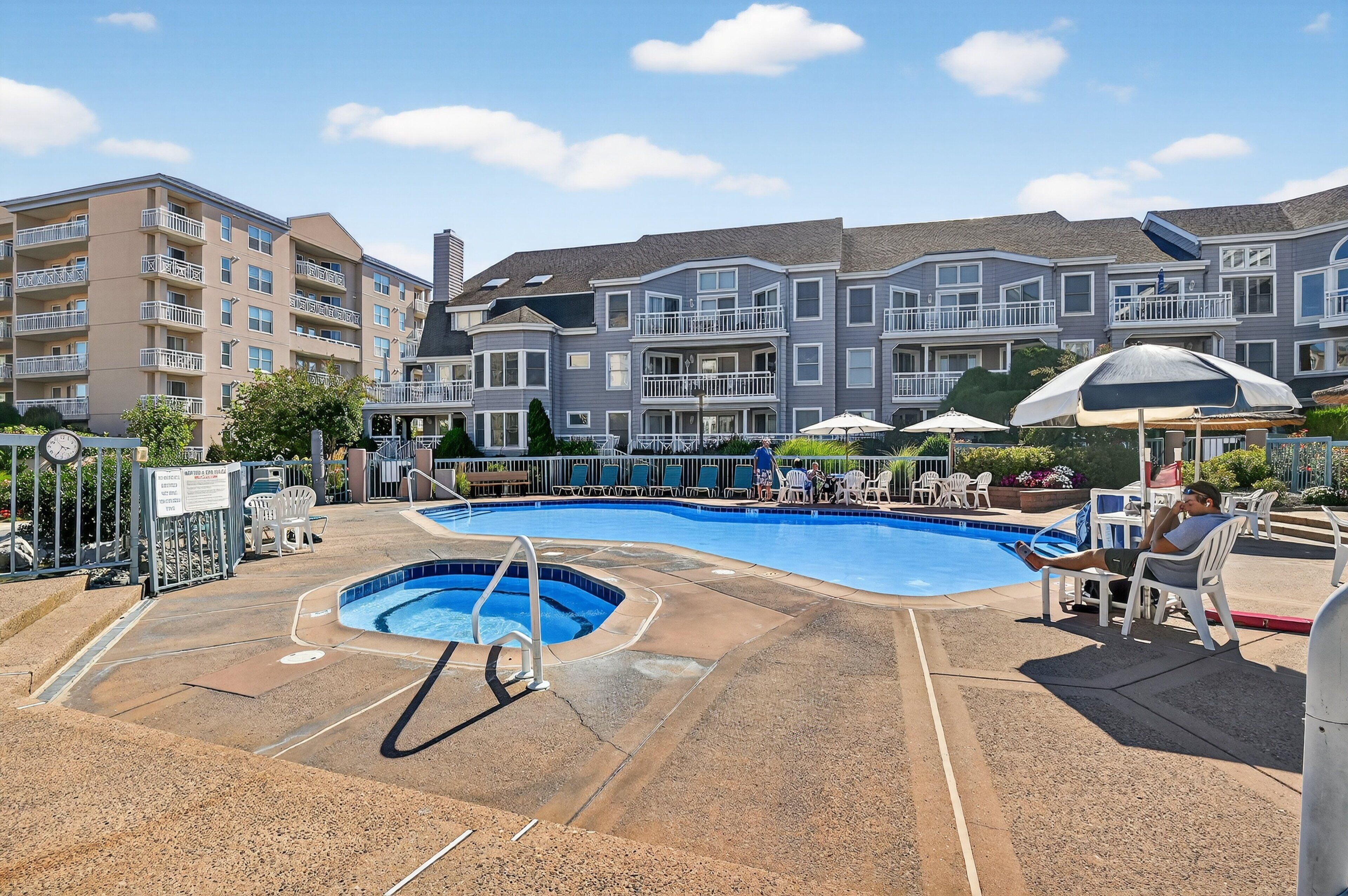A swimming pool area with a diving board, lounge chairs, and a building with multiple balconies in the background.