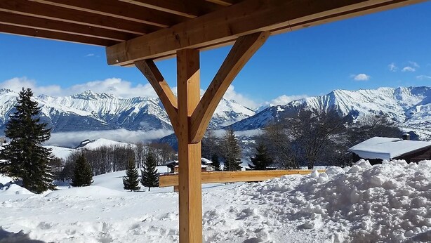 A wooden structure with a view of snow-covered mountains and trees.