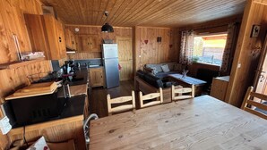 A wooden cabin interior with a kitchen, dining area, and seating space.