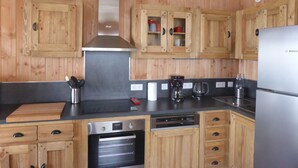 A kitchen with wooden cabinets, a stainless steel refrigerator, a built-in oven, and a hanging light fixture.