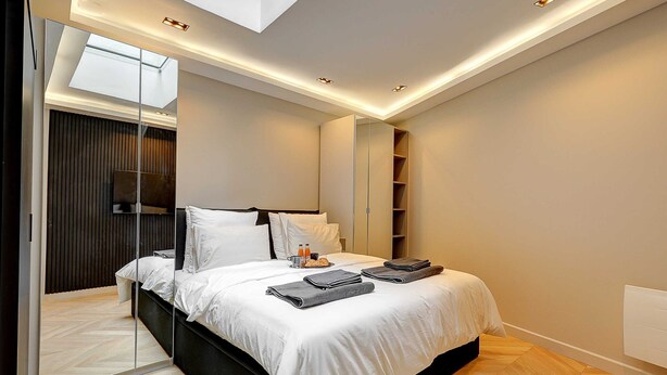 A modern bedroom with a large bed, a skylight, and built-in shelving. - Elegant Apartment With AC - 3br/10p- Le Marais (Paris)