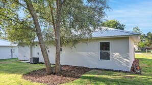 A small, single-story building with a white exterior, a tree in front, and a metal roof. - Sparkling 3-bedroom house with AC in Palatka (Palatka)