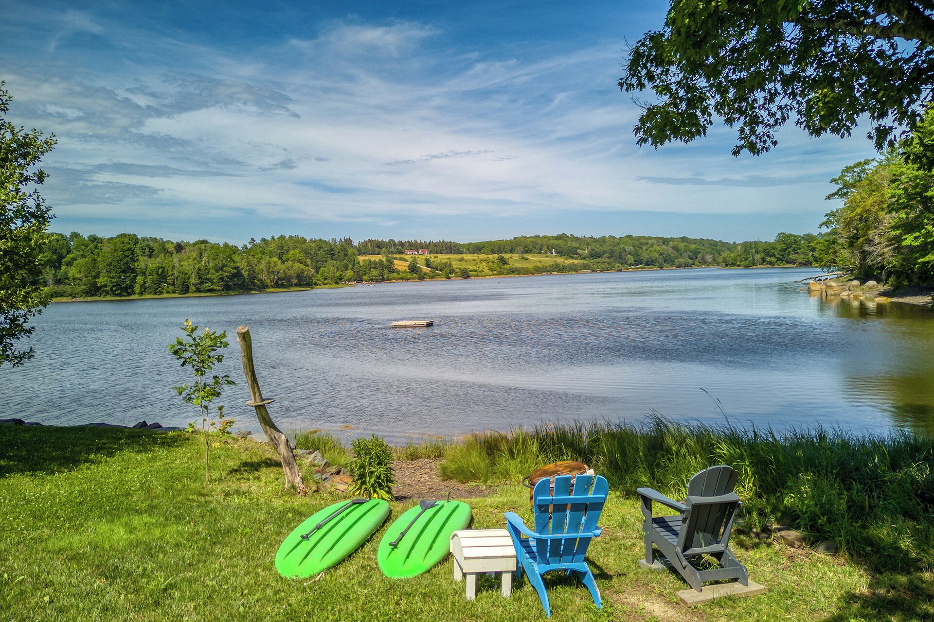 A lakeside view with a chair, paddleboards, and a small dock.