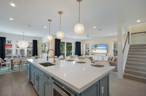 A spacious kitchen with a large island, pendant lighting, and a dining area with chairs and a table. - Amazing Beach House! 7 bedrooms, Heated pool, spa! (Bradenton Beach)