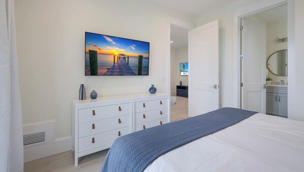 A bedroom with a bed, a dresser, a painting, and a bathroom visible through an open door.