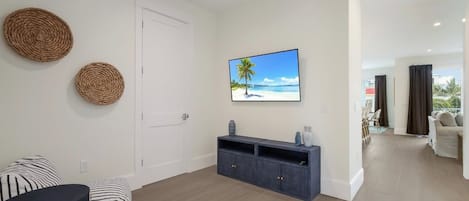 A modern living room with a sofa, a coffee table, a TV mounted on the wall, and a view of the beach through the window.
