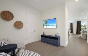A modern living room with a sofa, a coffee table, a TV mounted on the wall, and a view of the beach through the window.