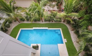 A rectangular swimming pool with a surrounding green lawn and palm trees. - Amazing Beach House! 7 bedrooms, Heated pool, spa! (Bradenton Beach)
