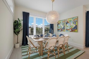 A dining area with a table set for four, a hanging light fixture, and abstract art on the wall. - Amazing Beach House! 7 bedrooms, Heated pool, spa! (Bradenton Beach)