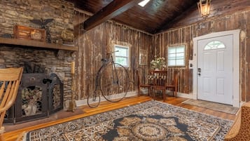 A rustic interior with a stone wall, wooden beams, a bicycle, a door, and a patterned rug.