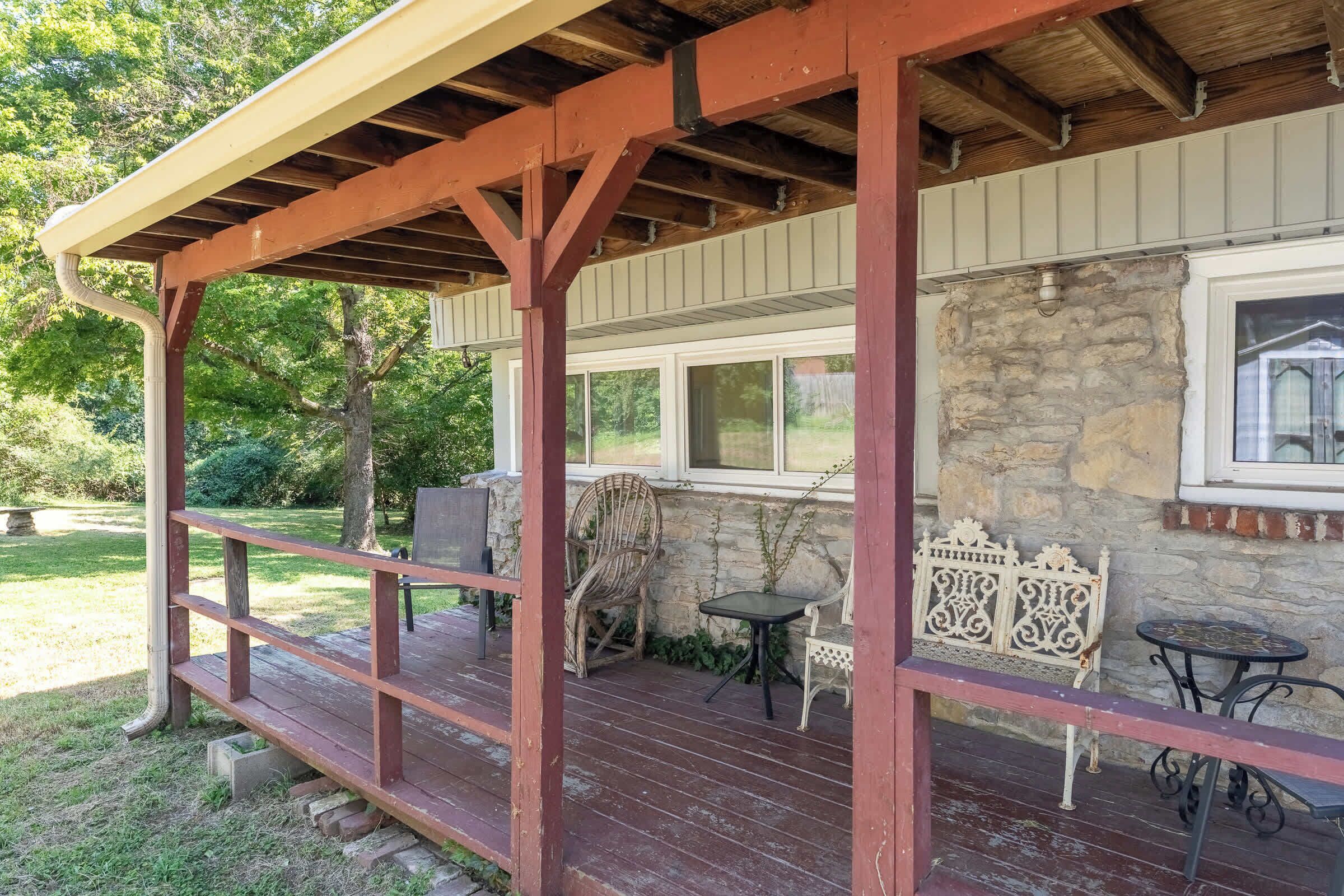 A covered outdoor area with a wooden deck, stone wall, and a window.