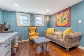 Une pièce avec un plancher en bois, un fauteuil jaune, un canapé à motifs, une petite table et une lampe fixée au mur.