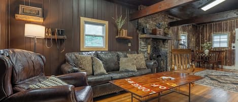 A cozy living room with a leather sofa, a wooden coffee table, and a stone wall.