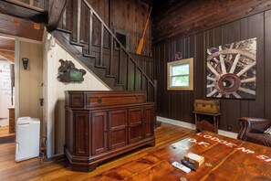 Une pièce avec un escalier en bois, une grande armoire en bois, une horloge murale rustique et une table en bois agrémentée d’un set de sous-verres.