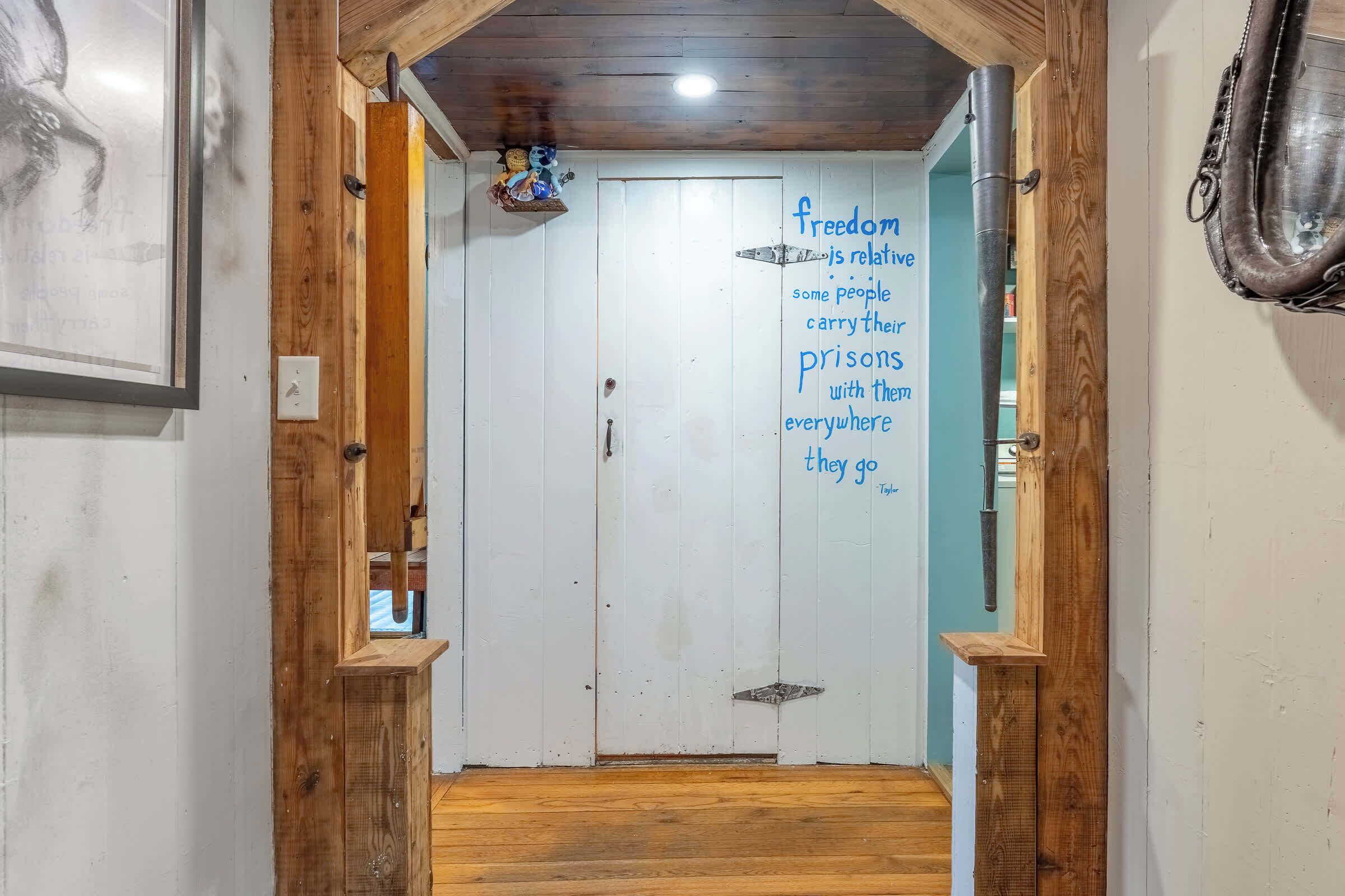 A hallway with a wooden door, a quote on the wall, and a metal pipe on the right.