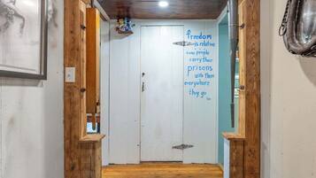 A hallway with a wooden door, a quote on the wall, and a metal pipe on the right.