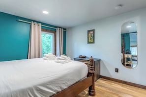 Ein Schlafzimmer mit einem Bett, einem Schminktisch, einem Spiegel und einem Fenster mit Vorhängen.