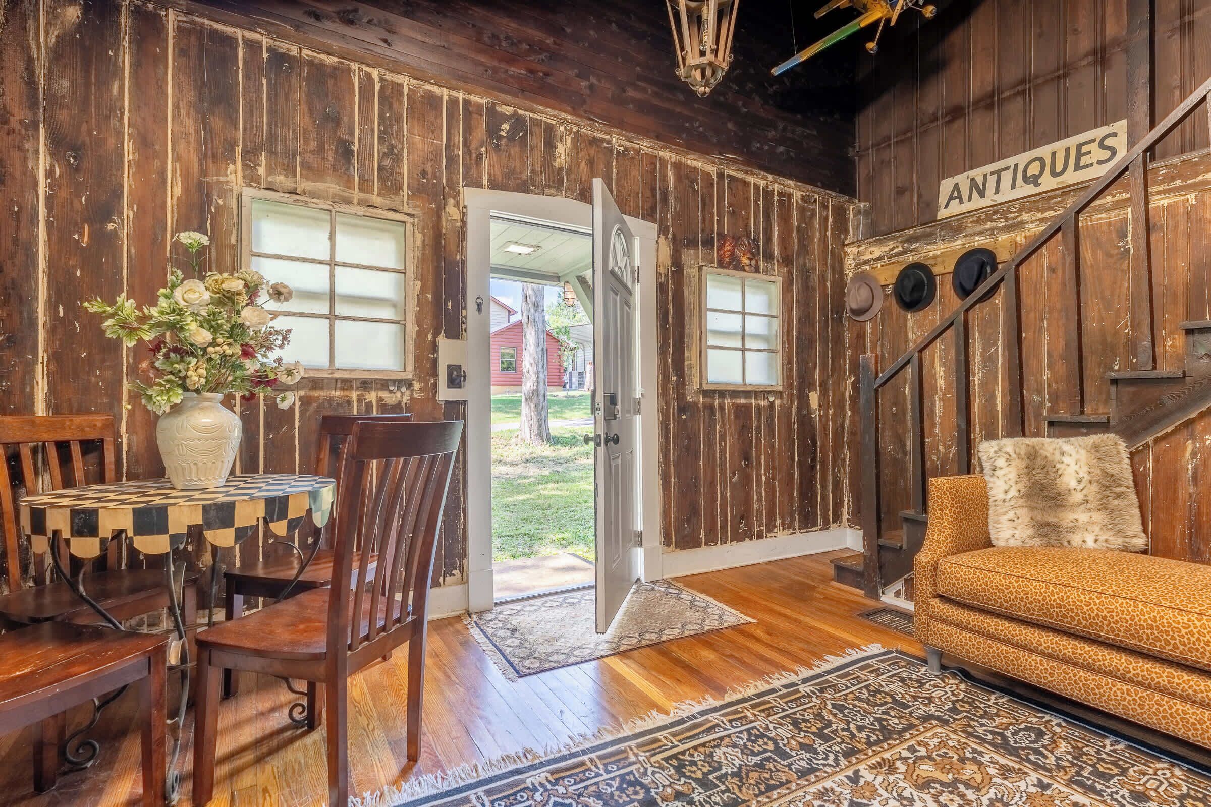 Un interior rústico con paredes de madera, una zona de comedor con una mesa de cuadros, un sofá y una alfombra.