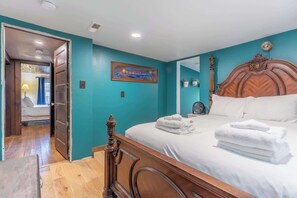 A bedroom with a wooden bed, a painting on the wall, and a door leading to another room.