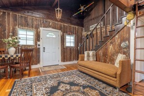 A rustic interior with a wooden staircase, a sofa, a dining table with chairs, and a chandelier.