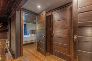 A hallway with wooden doors leading to a bedroom with a bed and a window.
