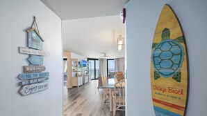 A hallway with a dining area, a wall with beach-themed decor, and a surfboard.
