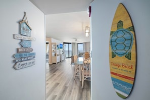 A hallway with a dining area, a wall with beach-themed decor, and a surfboard.