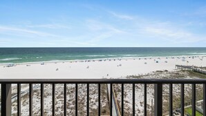 A beach view from a balcony with a railing, sandy beach, and ocean.