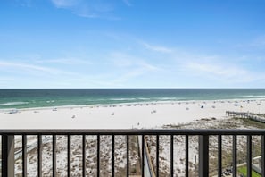 A beach view from a balcony with a railing, sandy beach, and ocean.