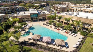 Een resort met een groot zwembad, omringd door ligbedden en parasols, moderne gebouwen en palmbomen.