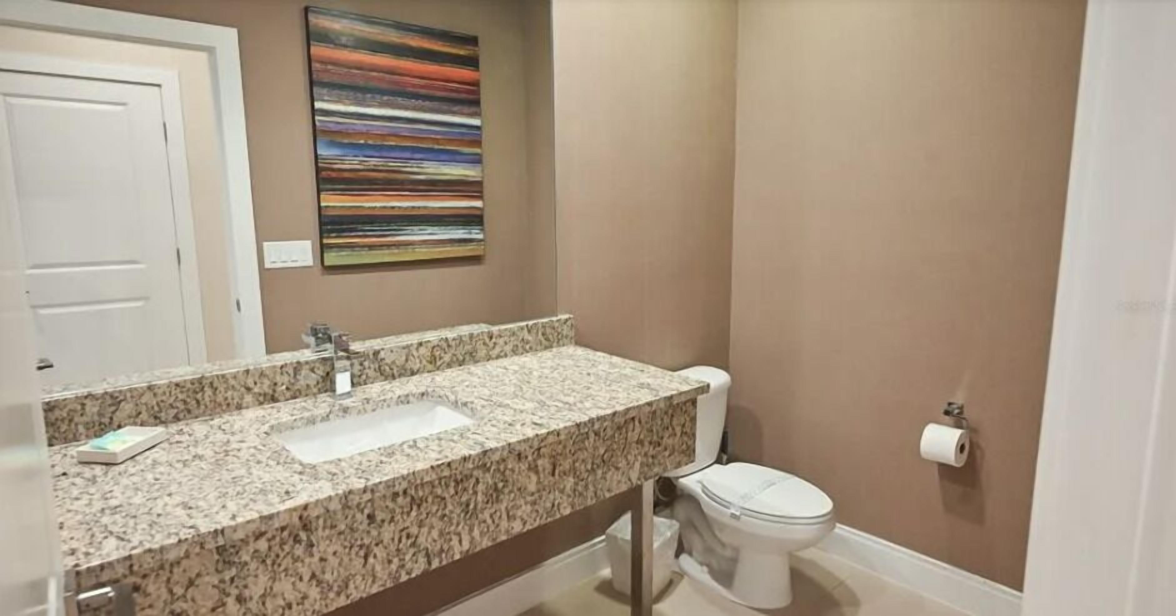 Une salle de bain avec un lavabo à vasque en granit, des toilettes blanches et un tableau abstrait aux couleurs vives accroché au mur.