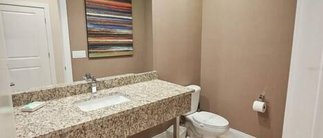 Une salle de bain avec un lavabo à vasque en granit, des toilettes blanches et un tableau abstrait aux couleurs vives accroché au mur.