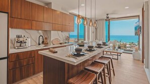 Una cocina moderna con armarios de madera, una isla central con taburetes y vista al océano.