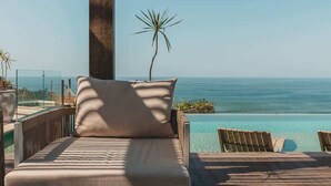 A balcony with a view of the ocean, a wooden deck, and a lounge chair.