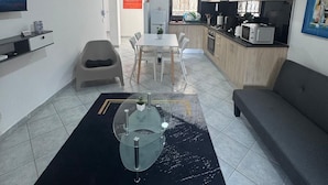 A modern living room with a dining area, a sofa, a TV, and a kitchen in the background.