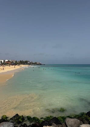 A beach with clear turquoise water, a sandy shore, and a few buildings in the background. - Refugio Hachi (8 people) (Santa Maria)