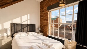 A bedroom with a large bed, a nightstand, a lamp, a window with a view of buildings, and a laundry bag. - City Centre Apt–Sleeps 6, Parking, Shops & Trains (Merseyside)